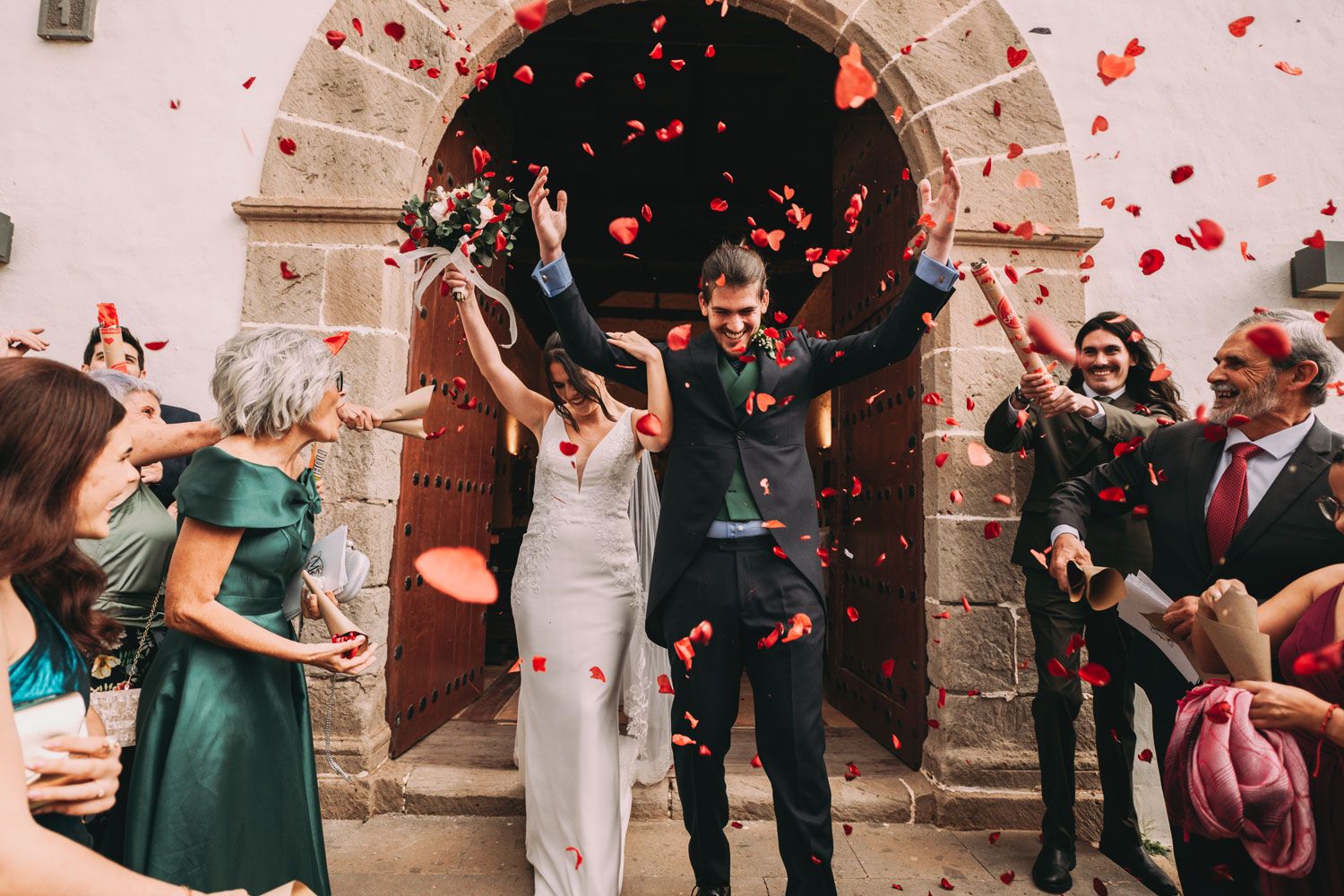 Boda en Madrid: novios saliendo de la iglesia entre pétalos de rosas rojas mientras los invitados celebran