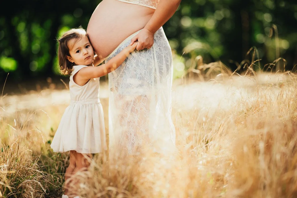Niña pequeña abraza la tripa de su madre embarazada durante una sesión de fotos al aire libre en Madrid