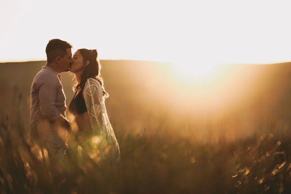 Pareja besándose al atardecer durante una sesión de fotos de embarazo en el campo, Madrid