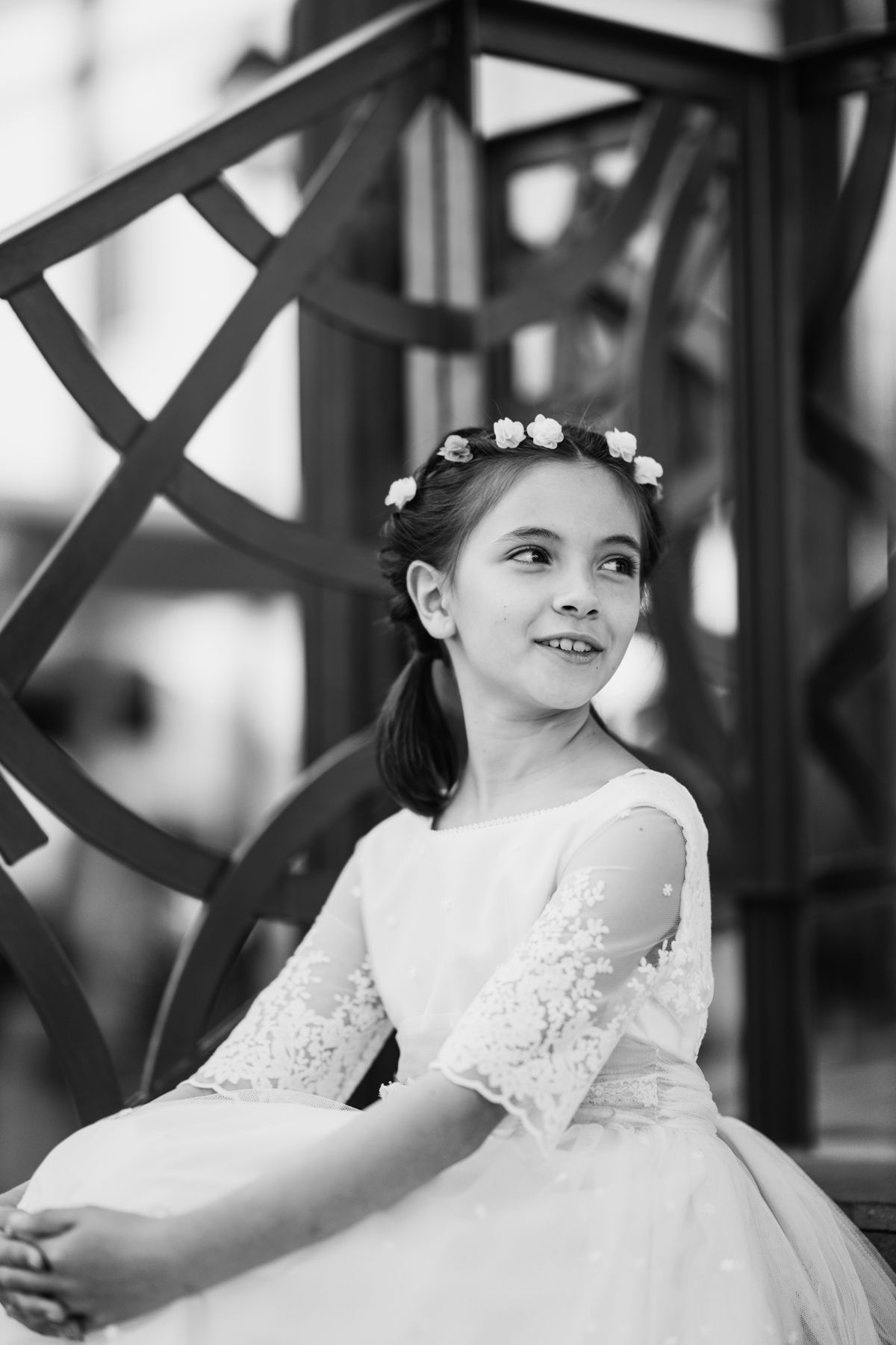 Retrato en blanco y negro de una niña de comunión sonriendo, sentada en un banco de forja