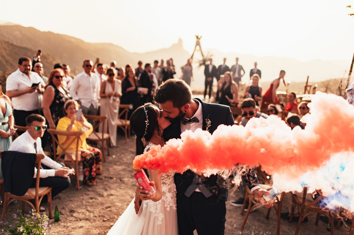 Boda boho al atardecer con humo de colores, ceremonia rodeada de invitados
