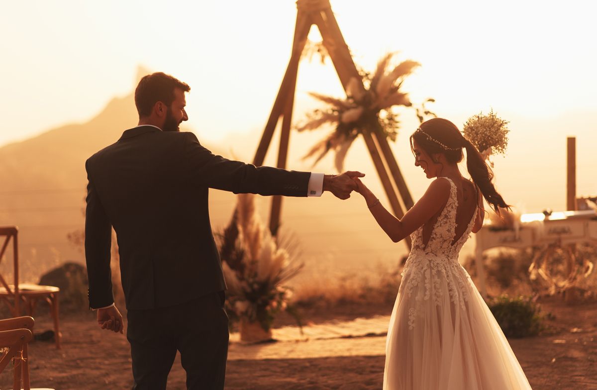 Novios cogidos de la mano al atardecer junto al altar boho de la ceremonia